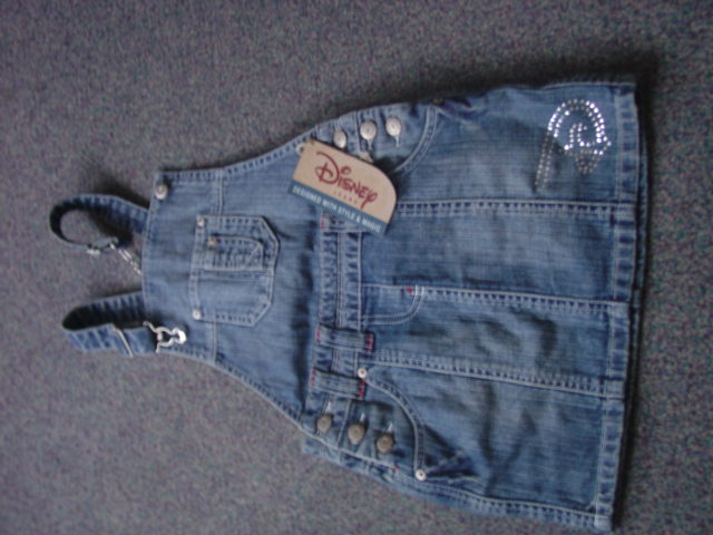 A WOVEN DENIM SKIRT FOR GIRLS.  WITH BIB AND BRACE AT THE CHEST AND BACK. DESIGNED TO COVER THE BODY FROM THE SHOULDERS TO MID THIGH. WITH SHOULDER STRAPS. WITH POCKETS FRONT AND BACK.  WITH APPLIED DIAMANTE DECORATION. WITH BUTTON FASTENING ON BOTH SIDES. HEMMED. 100 PER CENT COTTON.