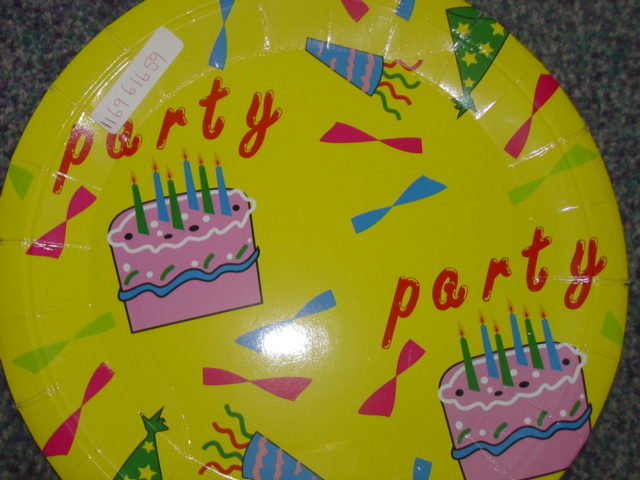 A PLATE MADE OF CARDBOARD DESIGNED FOR A CHILDRENS PARTY. THE PLATE IS YELLOW IN COLOUR AND IS DESIGNED WITH BIRTHDAY CAKES, HATS AND THE WORD PARTY PRINTED TWICE