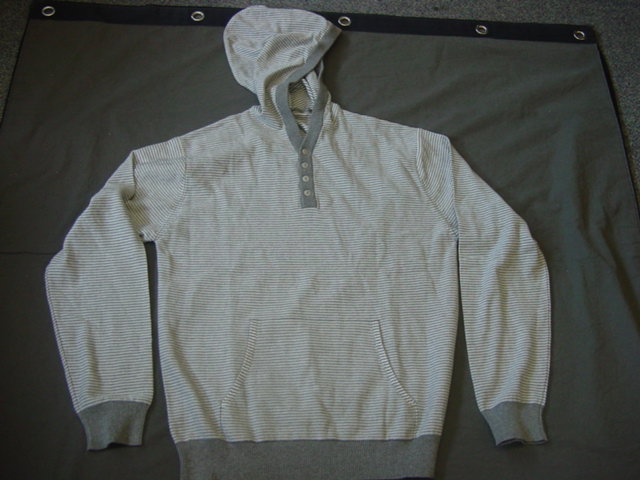 A KNITTED MENS PULLOVER. DESIGNED TO COVER THE UPPER PART OF THE CODY FROM THE SHOULDERS TO THE HIPS. WITH LONG SLEEVES. WITH HOOD. WITH 4 LEFT OVER RIGHT BUTTON PARTIAL OPENING. WITH KANGAROO POCKETS TO FRONT OF GARMENT. WITH RIBBING AT BASE AND CUFFS. THIN MATERIAL SO ABLE TO WEAR OUTER GARMENT OVER THE TOP. MADE FROM 100 PER CENT COTTON.