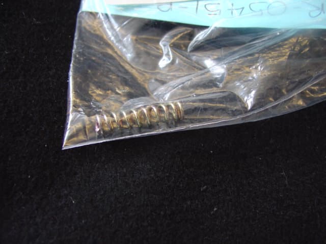 STEEL COIL COMPRESSION SPRING.  PLATED.  MEASURING 25MM LONG AND 6MM IN DIAMETER. PART OF RESTRAINT FOR WHEELCHAIR