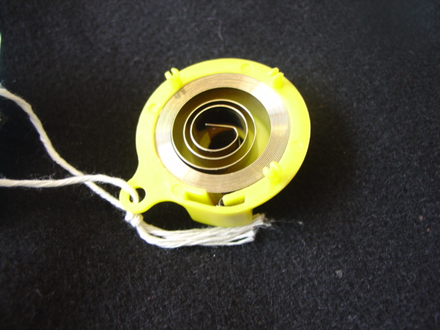 FLAT SPIRAL SPRING OF PLATED STEEL. IN YELLOW INJECTION MOULDED PLASTIC HOUSING.  SPRING DIAMETER 32 MM.  HOUSING DIAMETER: 42 MM.  HAS COMPANY NAME AND PART NUMBER STAMPED ON THE OUTSIDE OF THE HOUSING.  HOUSING HAS A HOLE IN THE CENTRE, DIAMETER  10 MM.  PART OF RESTRAINT FOR WHEELCHAIR