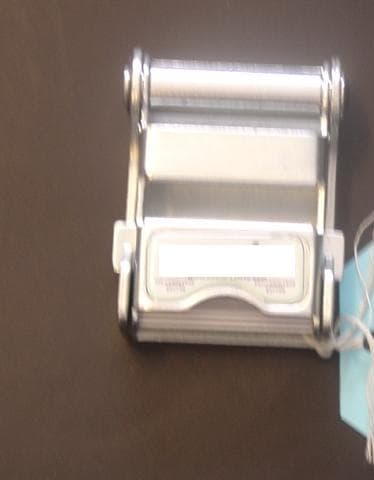 BUCKLE OF PRESSED STEEL. ELECTRO PLATED. WITH FASTENING MECHANISM. WITH COMPANY LOGO AND DETAILS ON TOP. PART OF RESTRAINT FOR WHEELCHAIR WHILST BEING TRANSPORTED