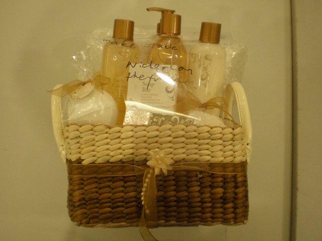 A RATTAN WICKER BASKET WITH HANDLES. MEASURING 23L x22W x 28H CM. WITH DECORATIVE BOW. PACKAGED TOGETHER WITH SOAP, CREME BATH, BODY LOTION, BODY WASH, HAND WASH PUMP, BODY SCRUB, BATH FIZZER, BATH SALT AND A PLASTIC PUFF ALL HAVE BEEN CLASSIFIED SEPARATELY.