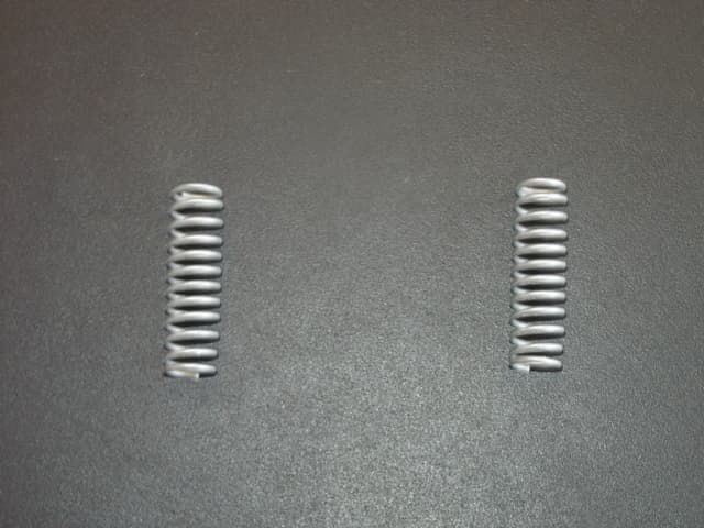 HELICAL COIL COMPRESSION SPRING. OF STEEL. USED AS PART OF THE MECHANISM OF A SEAT BELT BUCKLE.