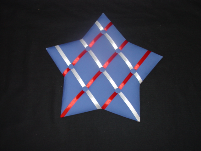 TEXTILE WALL HANGING. STAR SHAPED  MESSAGE BOARD. CONSTRUCTED  OF WOOD COVERED IN COTTON TEXTILE.  MEASURING APPROXIMATELY 42 CMS ACROSS FROM POINT TO POINT.  THE SURFACE IS PADDED  AND HAS RIBBONS ACROSS THE SURFACE HELD IN PLACE BY BUTTONS, FORMING SECTIONS FOR HOLDING PHOTOS OR MESSAGES IN. WITH METAL FIXTURE ON THE BACK FOR HANGING ON A WALL.
