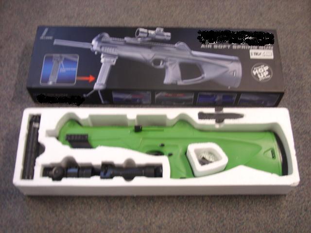 A SPRING POWERED AIR SOFT GUN WITH A GREEN ABS PLASTIC BODY AND BLACK ABS PLASTIC, ZINC OR ALLUMIUM PARTS.  FEATURES INCLUDE:  A SEE THROUGH PLASTIC MAGAZINE, A QUICK RELEASE BUTTON FOR THE MAGAZINE, A SILENCER, A DETACHABLE HANDLE REST AND A REAR AND FORE SIGHT FOR MOUNTING ON THE TOP.  IT ALSO FEATURES A HOP UP SYSTEM AND 6MM PROJECTILES.  OVERALL LENGTH (WITHOUT SILENCER ATTACHED) 65 CM.