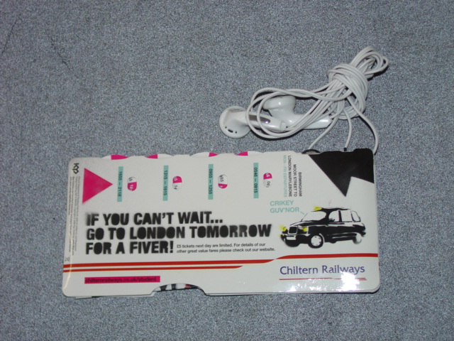 A RADIO INCORPORATED WITHIN A PAPERBOARD CASE PRINTED WITH ADVERTISING MATERIAL. WITH NON-REMOVEABLE HEADPHONES. WITH AN ON/OFF SWITCH. WITH A RESET BUTTON AND A SCAN BUTTON. WITH A TUNER DIAL. WITH LIMITED LIFE NON-REPLACEABLE BATTERY. WITH A REMOVEABLE PRINTED ADVERTISING LEAFLET FOR REDUCED TRAIN TRAVEL HELD INSIDE THE CASE. THE ESSENTIAL CHARACTER IS THAT OF THE RADIO. MEASURES 150MM X 70MM