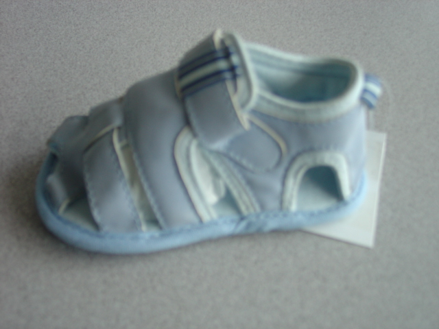 SANDAL FOR A BABY. NOT COVERING THE ANKLE.  UPPERS OF PLASTIC STRAPS ACROSS THE FRONT OF THE FOOT. WITH A VISIBLE TEXTILE LINING SHOWING AT THE ANKLE AND THE TOP OF THE SANDAL. ONE PLASTIC STRAP WITH VELCRO FASTENING. EMBROIDERED CAR MOTIFF SEWN ON THE STRAP END. WITH STRIPED FABRIC LOOP TO HOLD STRAP AT FRONT OF ANKLE. OUTER SOLE OF PLASTIC WITH PLASTIC DOTS. SOLE EDGED WITH TEXTILE BINDING. LIGHT BLUE IN COLOUR