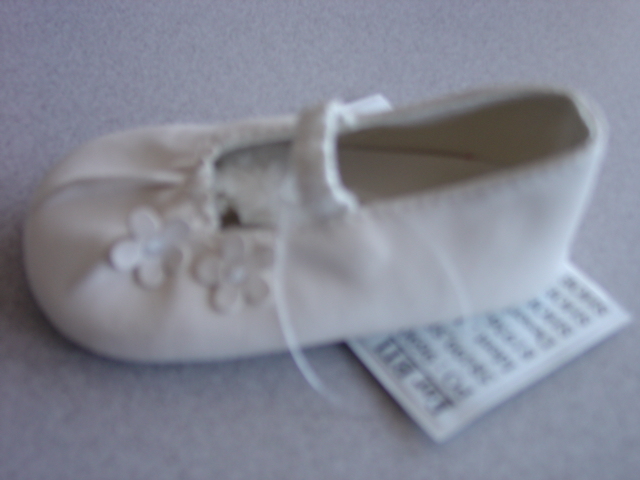 BABIES DOLLY STYLE SHOE. UPPERS OF PLASTIC. WITH FLORAL DECORATION. WITH ELASTICATED STRAP ACROSS THE FOREFOOT. OUTER SOLES OF TEXTILE MATERIAL WITH RAISED PLASTIC DOTS. TEXTILE IS PREDOMINANT MATERIAL IN CONTACT WITH THE GROUND. WHITE IN COLOUR.