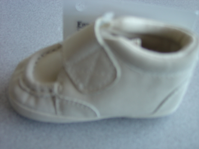 A LIGHT BROWN BABIES SHOE. WITH AN UPPER OF PLASTIC MOCK SUEDE AND OUTER SOLE OF TEXTILE AND PLASTIC PIMPLES WHERE THE TEXTILE PREDOMINATES. WITH ONE VELCRO FASTENING STRAP OVER THE INSTEP. WITH A CAR MOTIF STITCHED TO THE VELCRO STRAP.
