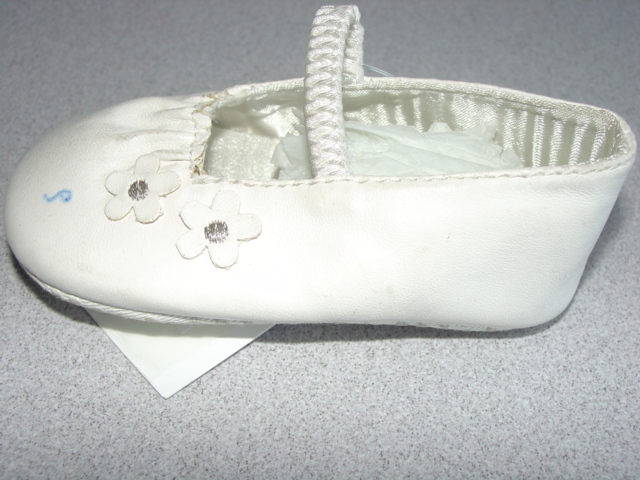 BABIES DOLLY STYLE INDOOR SHOE. UPPERS OF PLASTIC. WITH ELASTICATED STRAP ACROSS THE FOREFOOT.  OUTER SOLES OF TEXTILE MATERIAL WITH RAISED PLASTIC DOTS. TEXTILE IS PREDOMINANT MATERIAL IN CONTACT WITH THE GROUND. WHITE IN COLOUR.