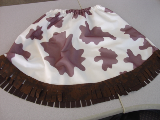 A KNITTED SKIRT OF MAN-MADE FIBRES WITH AN ELASTICATED WAISTBAND. WITH A COW HIDE PRINT IN BROWN AND WHITE. WITH A FRINGED HEM AT THE BASE. MEASURING 45CM FROM WAIST TO HEM. PACKAGED TOGETHER FOR RETAIL SALE WITH A CHILD'S FANCY DRESS COWGIRL OUTFIT. ALL ITEMS CLASSIFIED SEPARATELY.