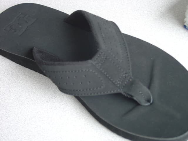 MENS FLIP FLOP. UPPER THONG OF LEATHER AND TEXTILE WHERE THE LEATHER IS THE OUTER SURFACE. WITH TOE POST SEPARATING THE FIRST AND SECOND TOE CONSTRUCTED OF LEATHER AND TEXTILE STRIPS.  THE LEATHER STRIP IS ATTACHED TO THE TEXTILE BY STITCHING AND GLUE AND COMPLETELY ENCIRCLES THE UPPER THONG.  THE TEXTILE STRIP IS ONLY STITCHED TO THE UNDERSIDE OF THE UPPER THONG VIA THE LEATHER STRIP.  NOT SECURED TO THE SOLE BY MEANS OF PLUGS.  OUTER SOLE OF RUBBER. INSOLE  LENGTH MORE THAN 24CMS. BLACK IN COLOUR.