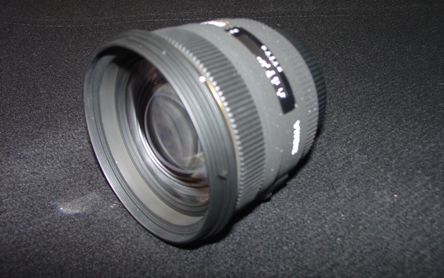 AN OBJECTIVE LENS FOR A PHOTOGRAPHIC CAMERA. OF GLASS, METAL AND PLASTIC. WITH A  FIXED FOCAL LENGTH OF 50MM AND A FRONT DIAMETER OF 77MM. WITH REMOVABLE PLASTIC LENS CAPS. LENS LENGTH 68.2 MM. WEIGHT 505G.