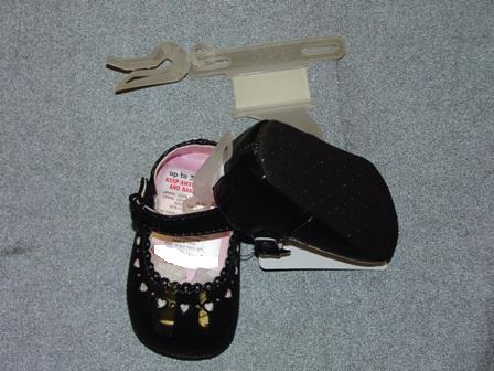 BABIES INDOOR SHOE, FOR UP TO 3 MONTHS. WITH UPPERS OF PLASTIC.  WITH VELCRO STRAP FASTENING WITH MOCK BUCKLE. WITH SMALL HEART SHAPED CUT OUTS ON UPPER. OUTER SOLES OF TEXTILE MATERIAL WITH RAISED PLASTIC DOTS. TEXTILE IS PREDOMINANT MATERIAL IN CONTACT WITH THE GROUND. BLACK.  PRESENTED ON A LITTLE PLASTIC HANGER WITH CARD LABEL