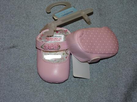 BABIES INDOOR SHOE, FOR UP TO 3 MONTHS. WITH UPPERS OF PLASTIC.  WITH VELCRO STRAP FASTENING. WITH APPLIED DECORATION OF TEXTILE ROSES ON STRAP. OUTER SOLES OF TEXTILE MATERIAL WITH RAISED PLASTIC DOTS. TEXTILE IS PREDOMINANT MATERIAL IN CONTACT WITH THE GROUND. PINK IN COLOUR.  PRESENTED ON A LITTLE PLASTIC HANGER WITH CARD LABEL