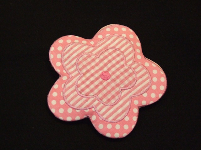 TEXTILE WALL HANGING. PETAL SHAPED TEXTILE MOTIF WITH HARD PLASTIC BACK, AND HOOK FOR HANGING ON THE WALL. MEASURING APPROXIMATELY 15 CMS ACROSS FROM POINT TO POINT.