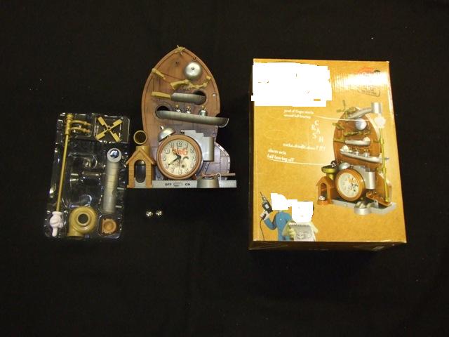 A BATTERY OPERATED PLASTIC ALARM CLOCK WHICH USES A SERIES OF GRAVITY AND BALL BEARINGS TO SET THE ALARM OFF. THE CLOCK INCLUDES INSTRUCTIONS FOR SETTING THE CLOCK UP AND SETTING THE TIME . THE TWO BALL BEARINGS ARE PLACED IN CERTAIN POSITIONS AND WHEN RELEASED TRIGGER THE ALARM OFF WITH WIND CHIMES, CYMBALS AND EVEN A COCKEREL. IF THE DOG BOWL IS REMOVED THE BALL BEARING IS SET OFF ON A MAD COURSE OF YOUR OWN INVENTION.  INCLUDES ON AND OFF SWITCH. COMPONENTS COMPRISE ALARM CLOCK BODY, CRACKING HAND, LOADING SLIDE, 2 BALL BEARINGS, WINDMILL, DOG BOWL AND VORTEX. PACKAGED FOR RETAIL SALE IN A CARDBOARD BOX.