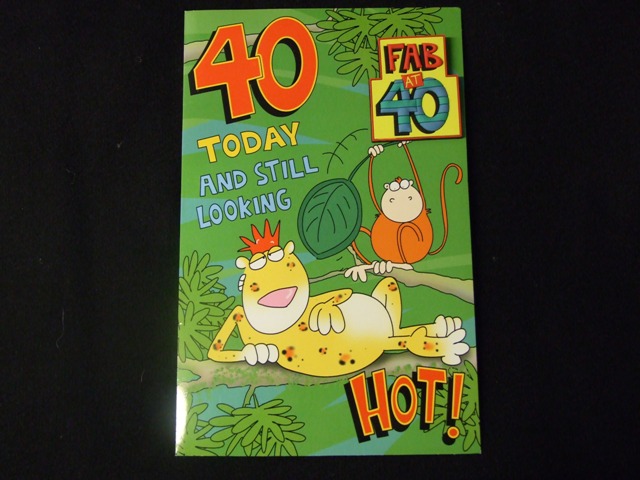 PRINTED PAPERBOARD 40TH BIRTHDAY CARD. WITH PRINTED  PICTURE ON FRONT OF CARD. PRINTED 40TH BIRTHDAY GREETING ON FRONT OF CARD  AND PRINTED MESSAGE INSIDE.ATTACHED TO THE FRONT OF THE CARD IS AN EMBOSSED 40TH PLASTIC PIN BADGE. WITH ENVELOPE.