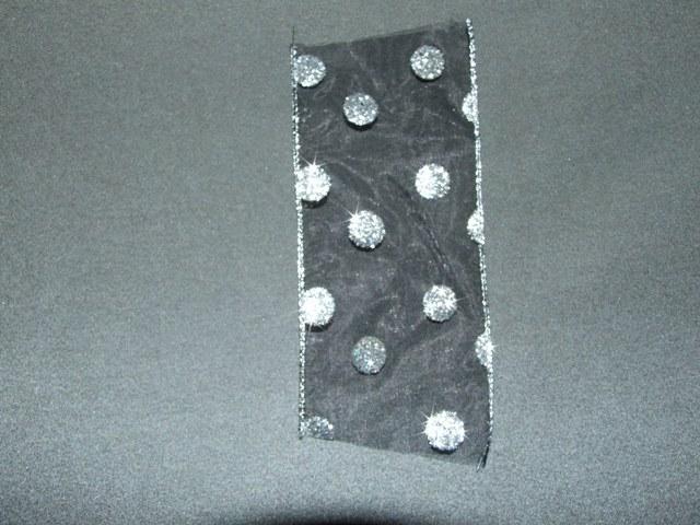 A NARROW WOVEN BLACK FABRIC OF MAN MADE FIBRES, POLYESTER. MEASURING 6CMS IN WIDTH. HEMMED AT EDGES WITH A SILVER METALLISED YARN AND REINFORCED WITH METAL WIRE. DECORATED WITH A SILVER GLITTER CIRCLES. PACKAGED FOR RETAIL SALE ON REELS AND IS PACKAGED IN A POLYBAG.