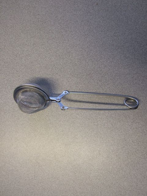 HAND HELD TEA INFUSER/STRAINER. OF STAINLESS STEEL. WITH 2 SEMI CIRCULAR DOMES OF WIRE MESH. ATTACHED TO A SPRING STYLE HANDLE.  WHEN PRESSING THE HANDLE THE DOMES OPEN UP ALLOWING TEA TO BE PLACED INTO THEM. WHEN RELEASED THE DOMES CLOSE AND HOLD THE TEA IN PLACE.