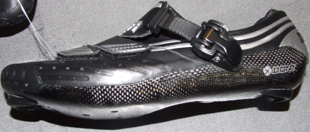 A CYCLING SHOE. THE SHOE IS MADE FROM THE INSIDE OUT. EVERYTHING IS LAMINATED TOGETHER BY THE EPOXY RESIN SO IT FORMS A MONOCOQUE. CARBON FIBRE IS THEN HAND LAYED. AIRCRAFT GRADED CARBON IS WEAVED ON THE OUTSIDE AND UNDIRECTIONAL CARBON ON THE INSIDE. THE UNI DIRECTIONAL CARBON HAS ONLY HALF THE STRANDS OF CROSS WEAVE CARBON. IT GIVES STRENGTH IN ONE DIRECTION SO IT SAVES WEIGHT BY USING LESS CARBON OF ABSORBING LESS RESIN. BLACK AND SILVER IN COLOUR