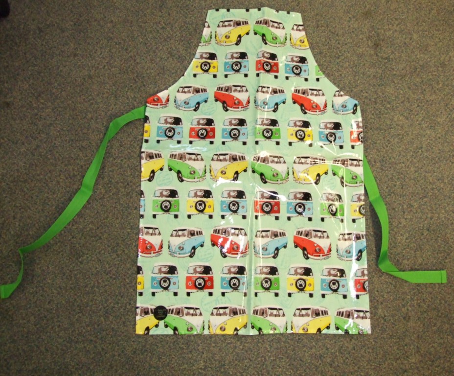 A WOVEN APRON FOR CHILDREN. COVERING THE FRONT OF THE BODY.  WITH A STRAP FOR WEARING AROUND THE NECK, AND TWO STRAPS EXTENDING FROM THE SIDES FOR FASTENING AROUND THE BACK. WITH A NON- VISIBLE PVC COATING ON THE OUTER SURFACE OF THE FABRIC. WITH PRINTED DESIGN.  OF 100% COTTON.