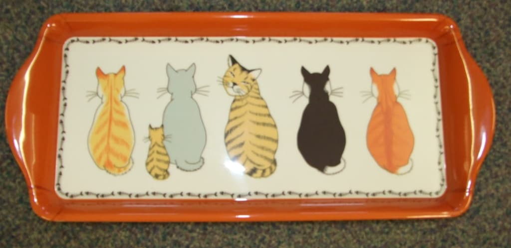 A PLASTIC MELAMINE TRAY . DESIGNED FOR DOMESTIC/HOUSEHOLD USE. THE TOP IS DECORATED WITH A CAT DESIGN. THE DIMENSIONS OF THE BASE OF THE TRAY ARE APPROX 32CM LENGTH X 14CM WIDTH.