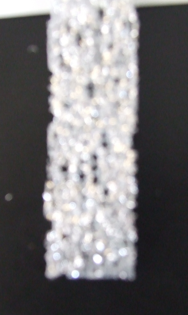 KNITTED COATED FABRIC. A NARROW DECORATIVE TRIMMING. WITH A BASE OF WHITE KNITTED FABRIC COATED ON ONE SIDE IN FINE SPARKLY SILVER FIBRES. 23MM WIDE. 100% POLYESTER. PRESENTED AS PART OF A MIXED SET OF KNITTED AND WOVEN TRIMMINGS AND RIBBONS. ALL CLASSIFIED SEPARATELY.