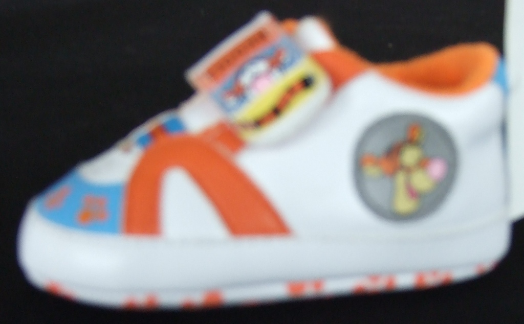 INDOOR FOOTWEAR. BOOTEE IN THE STYLE OF A TRAINER DESIGNED FOR A BABY. WITH UPPERS OF PLASTIC (PU) AND OUTER SOLES OF TEXTILE WITH PLASTIC (PU) RAISED PRINT, WHERE THE TEXTILE PREDOMINATES. DOES NOT COVER THE ANKLE. WITH SINGLE VELCRO STRAP FASTENING. WITH A FAMOUS CHILDRENS STORY BOOK CHARACTER ON SHOE. WITH FACE OF CHARACTER ON SIDE OF THE SHOE AND ON THE VELCRO STRAP. WITH THE LETTER 'T' ON THE SOLE OF THE SHOE. WHITE AND ORANGE IN COLOUR.