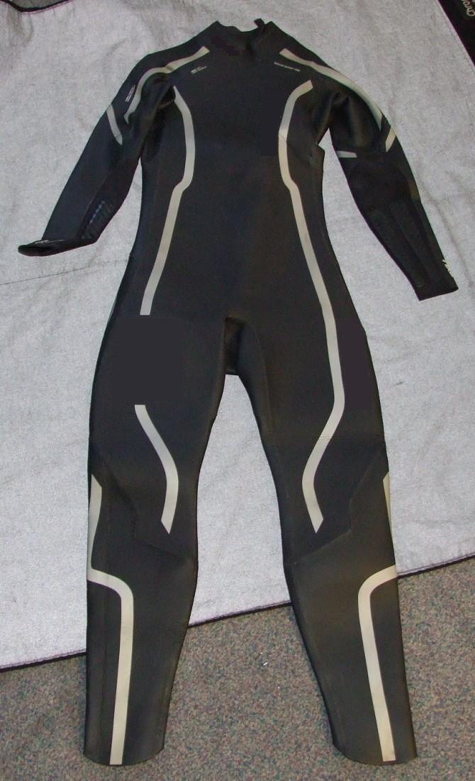 A ONE-PIECE WET SUIT FOR ADULTS.  MADE OF CELLULAR NEOPRENE RUBBER.  DESIGNED TO COVER THE ENTIRE BODY FROM ANKLE TO NECK, WITH LONG SLEEVES.  WITH A ZIP CLOSURE AT THE BACK AND VELCRO FASTENING AT THE TOP TO COVER THE ZIPPER.  THE WET SUIT IS BLACK WITH SILVER AND WHITE PRINTING.  THE NEOPRENE HAS A KNITTED LINING; HOWEVER THIS IS PRESENT FOR REINFORCEMENT ONLY.