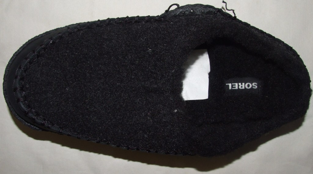 A MAN'S MULE STYLE SLIPPER COVERING THE TOP AND  PART OF THE SIDE OF THE FOOT.THE UPPER COMPRISES TEXTILE MATERIAL COVERING THE TOP AND PART OF THE SIDE OF THE FOOT AND LEATHER COVERING THE REST OF THE SIDE OF THE FOOT. THE SLIPPER  HAS A TEXTILE FAKE FUR LINING AND THE SOLE IF MADE OF RUBBER. THE PREDOMINANT MATERIAL OF THE UPPER IS LEATHER.