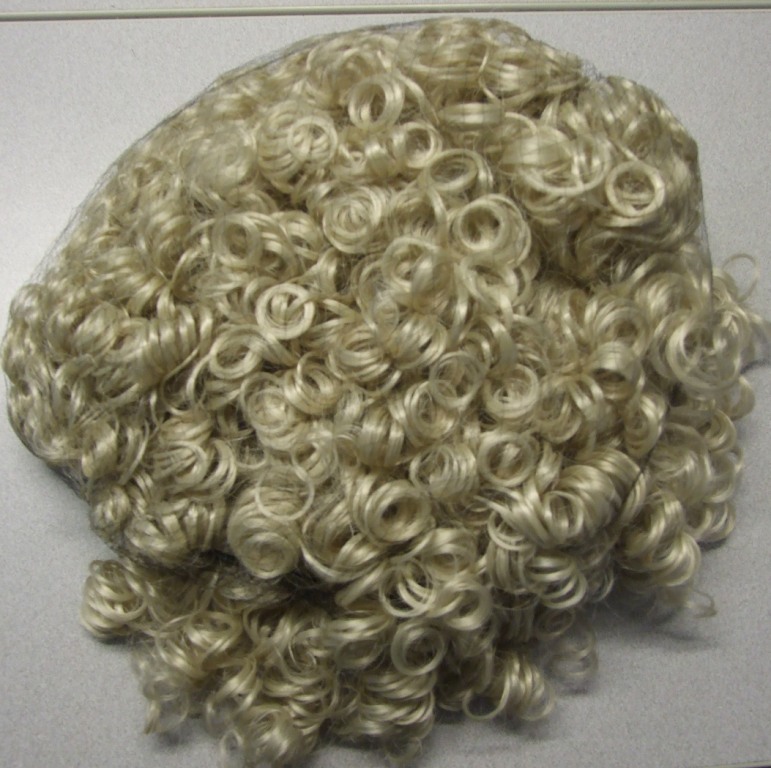 A COMPLETE WIG MADE OF SYNTHETIC TEXTILE MATERIALS DESIGNED FOR A DANCER. THE WIG HAS RINGLETS AND IS WELL MADE WITH A LACE CAP AND PLASTIC COMBS BOTH SIDE OF THE WIG WHICH ATTACH TO THE HEAD.