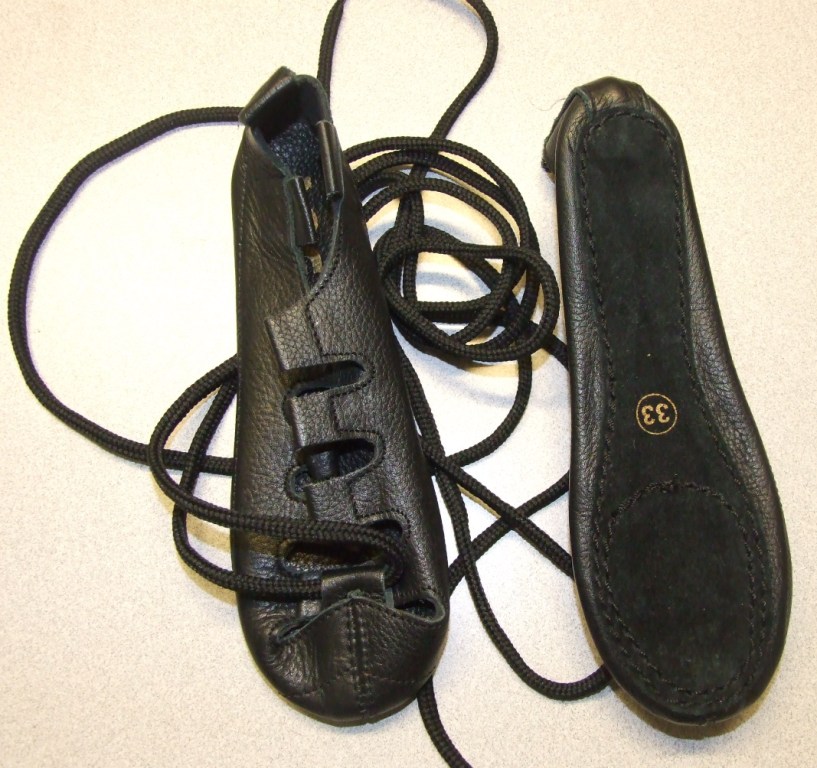 CHILDS DANCING PUMP. UPPER OF LEATHER AND SOLE OF LEATHER (SUEDE). THE PUMP HAS A LACE UP FASTENING WITH A TOTAL OF EIGHT EYELETS TO THREAD THE LACES THROUGH. BLACK IN COLOUR. IN-SOLE LENGTH LESS THAN 24CMS. NOT COVERING THE ANKLE. WITH A LOOP AT THE BACK OF THE HEEL.