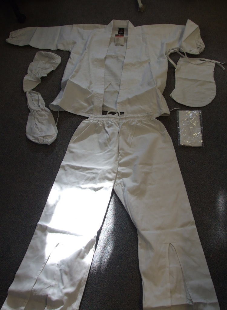 A WOVEN KARATE ENSEMBLE FOR UNISEX. UPPER GARMENT IS A WRAP-OVER STYLE
JACKET, WHICH FASTENS WITH TIES IN EITHER DIRECTION. WITH INSIDE AND OUTER TIES.. 
WITH LONG SLEEVES.  ELASTICATED AT SLEEVE ENDS. HEMMED AT BASE OF GARMENT. WITH SIDE VENTS.
TROUSERS HAVE AN ELASTICATED WAIST, WITH A CONCEALED DRAWSTRNG.  WITH SLITS TO THE LEGS AT BASE OF THE TROUSERS. WITH TIES AT THE TOP OF EACH SLIT AND JUST ABOVE THE HEMS OF THE TROUSERS. HEMMED AT LEG ENDS. 100% COTTON. WITH SMALL LOGO ON LEFT HAND CORNER OF JACKET WHICH IS REPLICATED AT THE WAIST ON THE TROUSERS. PACKAGED WITH A WOVEN HOOD WHICH TIES UNDER THE CHIN, A KNITTED FACE MASK WHICH PULLS OVER THE HEAD AND HAS A SLIT CUT OUT FOR THE EYES. ALSO PACKAGED WITH WOVEN TEXTILE GAUNTLETS  THAT COVER THE HAND AND REACH TO THE ELBOW.  ALL ITEMS MADE OF 100% COTTON