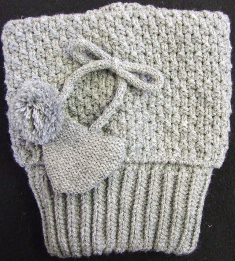 A LADIES BASKET WEAVE KNITTED BOOT TOPPER WITH HEART AND POM POM BOW.  IT IS DESIGNED TO BE WORN AROUND THE LEG AND COVER THE TOP OF THE BOOT FOR DECORATIVE PURPOSES.  IT DOES NOT COVER THE FOOT.  ITEM IS MADE FROM 100% ACRYLIC.