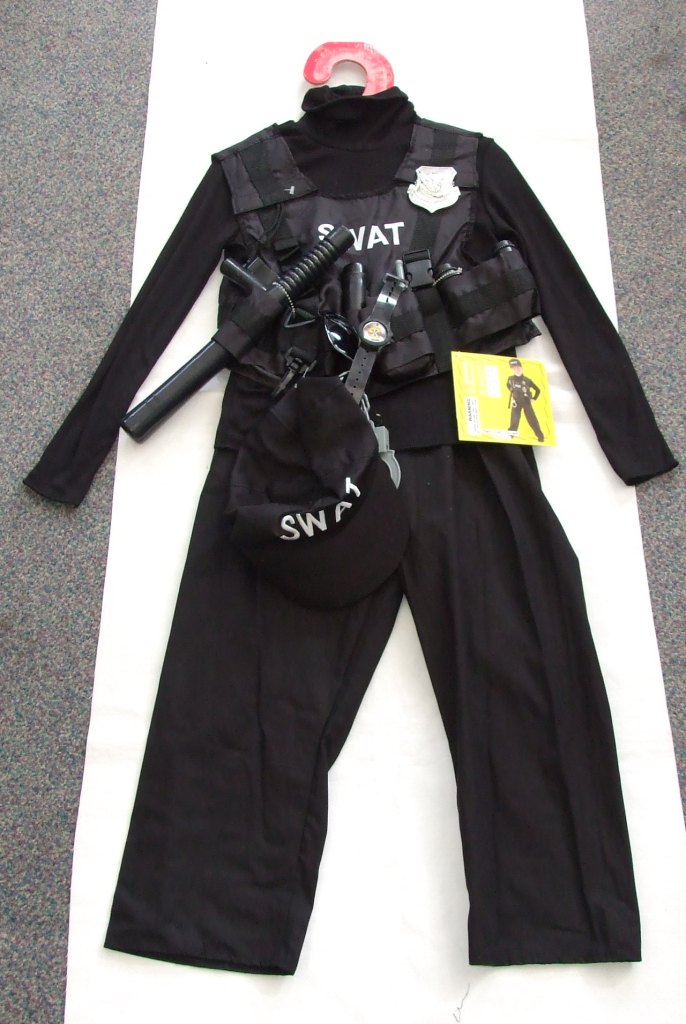 UNISEX WOVEN TROUSERS. PART OF A FANCY DRESS SWAT TEAM OUTFIT FOR CHILDREN. MADE FROM COTTON. DESIGNED TO COVER THE LOWER PART OF THE BODY FROM THE WAIST TO THE ANKLES. ENVELOPING EACH LEG SEPARATELY. PULL ON IN DESIGN WITH ELASTICATED WAISTBAND AND NO FASTENING. HEMMED AT THE LEG ENDS. PRESENTED FOR RETAIL SALE ON A CARDBOARD HANGER WITH A TEXTILE PULLOVER, HAT, VEST AND PLASTIC ACCESSORIES ALL CLASSIFIED SEPARATELY. WITH A PRINTED SWING TAG.