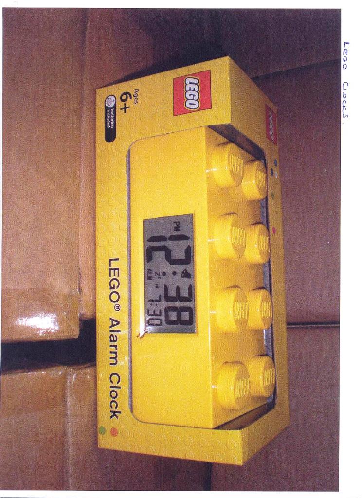 LEGO ALARM BRICK CLOCK. A DIGITAL DISPLAY CLOCK HOUSED IN A LEGO BUILDING BRICK. THE FINISHED PRODUCT HAS A LEGO FIGURE ATTACHED ON TOP SO THAT THE RETAIL ITEM IS SOLD AS, FOR EXAMPLE, SUPERMAN LEGO CLOCK.