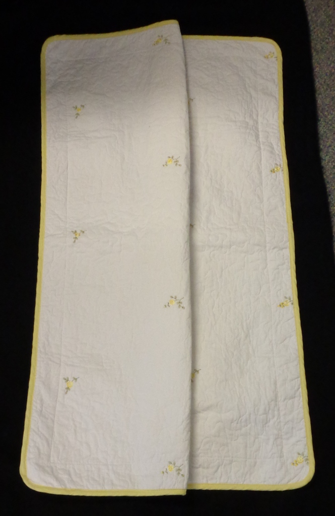A PILLOW SHAM. RECTANGULAR IN SHAPE MEASURING APPROX 56  X 84CMS. CONSISTING OF A FRONT PANEL OF WOVEN, QUILTED 100% COTTON WITH EMBROIDERED ROSEBUD  DESIGN AND A PLAIN WOVEN REVERSE SIDE OF 100%  COTTON.  THE QUILTED FRONT PANEL HAS A MIDDLE LAYER OF 100% COTTON.  THE FRONT AND BACK PANELS ARE JOINED TOGETHER ITO CREATE A POCKET INTO WHICH A PILLOW CAN BE INSERTED. LEMON PIPING AROUND THE EDGE AND LEMON ROSEBUD DESIGN.