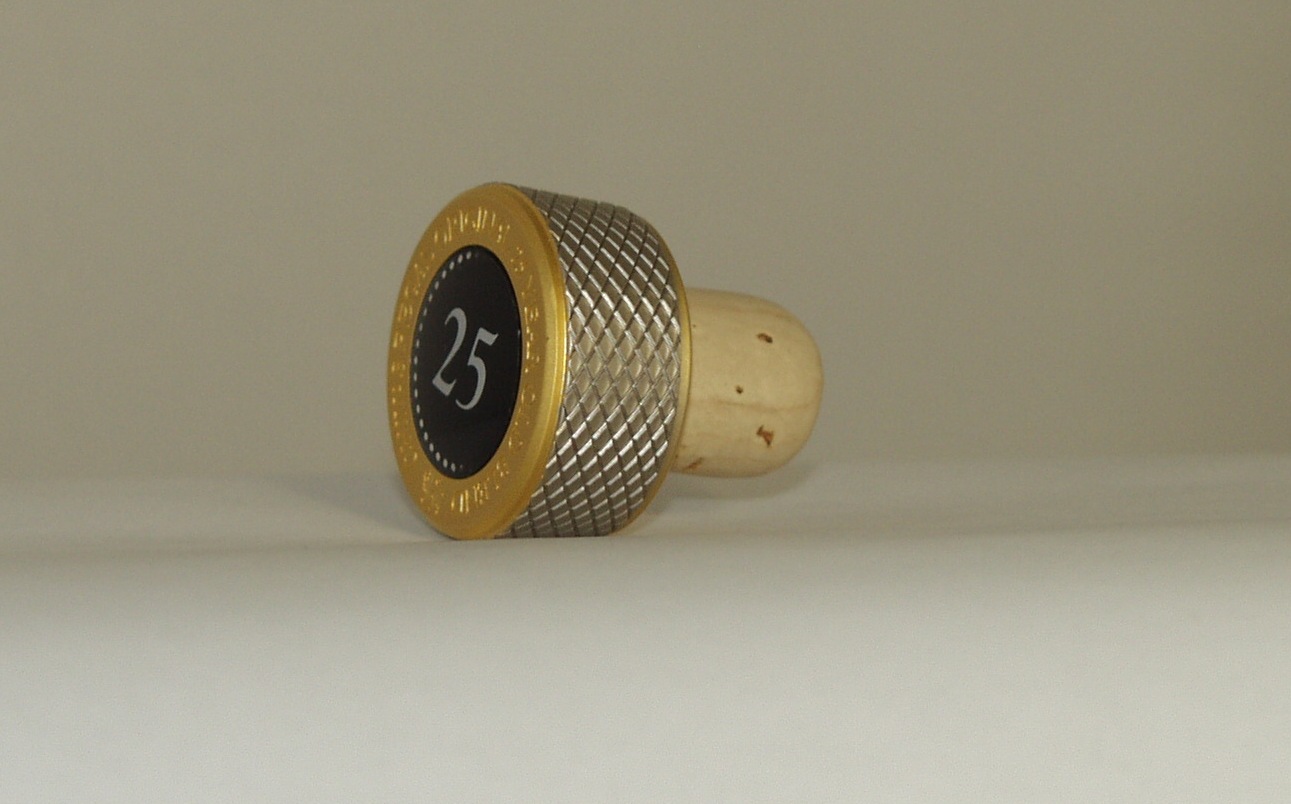 A  METAL BOTTLE STOPPER WITH BUILT IN CORK. WITH THE NUMBER 25 PRINTED ON THE TOP AND GOLD PLATED EDGE. DESIGNED TO BE PUT INTO BOTTLES OF WHISKY THAT ARE 25 YEARS OLD. MEASURES APPROX 35MM X 28MM.