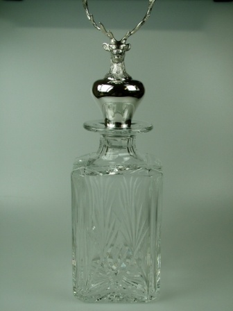 A LEAD CRYSTAL GLASS DECANTER WITH A LEAD CRYSTAL GLASS STOPPER CLAD WITH A DECORATIVE STERLING SILVER STAGS HEAD. THE LEAD CRYSTAL IS GATHERED BY HAND.