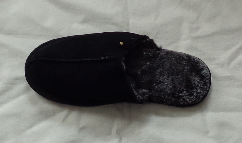 A MULE TYPE SLIP ON SLIPPER, NOT COVERING THE ANKLE. WITH A BLACK UPPER OF SUEDE. TEXTILE COVERED PU OUTER SOLE WITH A RIBBED PATTERN FOR GRIP. THE TEXTILE SOLE HAS DURABLE WEARING PROPERTIES AND IS CONSIDERED TO BE THE VIABLE OUTER SOLE. THE SLIPPER ALSO FEATURES A SOFT FUR-LIKE INNER. WITH AN INSOLE LENGTH OF MORE THAN 24 CMS.