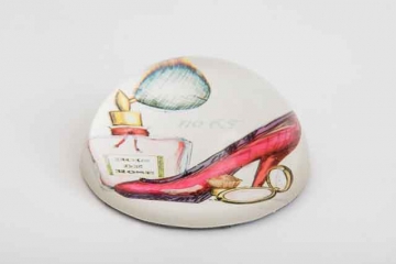 GLASS PAPER WEIGHT OF LAMP WORKED GLASS. THE BASE CONTAINS A PICTURE OF A LADY'S SHOE, PERFUME BOTTLE AND A COMPACT WHICH IS REFLECTED WITHIN THE GLASS.