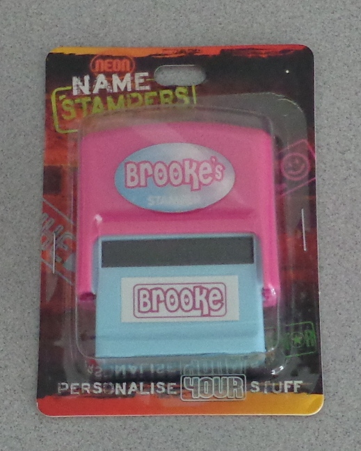 SELF INKING STAMPER. DESIGNED FOR OPERATING IN THE HAND. THE ARTICLE PRODUCES A PERSONALISED NAME WHEN DEPRESSED.  THE ARTICLE IS MADE OF PLASTIC AND IS COLOURED PINK AND LIGHT BLUE.  WHEN THE STAMP IS DEPRESSED THE NAMING/SUBJECT PLATE OF THE STAMP IS RELEASED FROM AN INTERNAL INK PAD AND SPUN ON ITS OWN AXIS TO PRINT ONTO A SURFACE. ONCE THE STAMP IS RELEASED, THE NAMING SUBJECT PART RETURNS TO ITS ORIGINAL POSITION IN TOUCH WITH THE INTERNAL INK PAD.