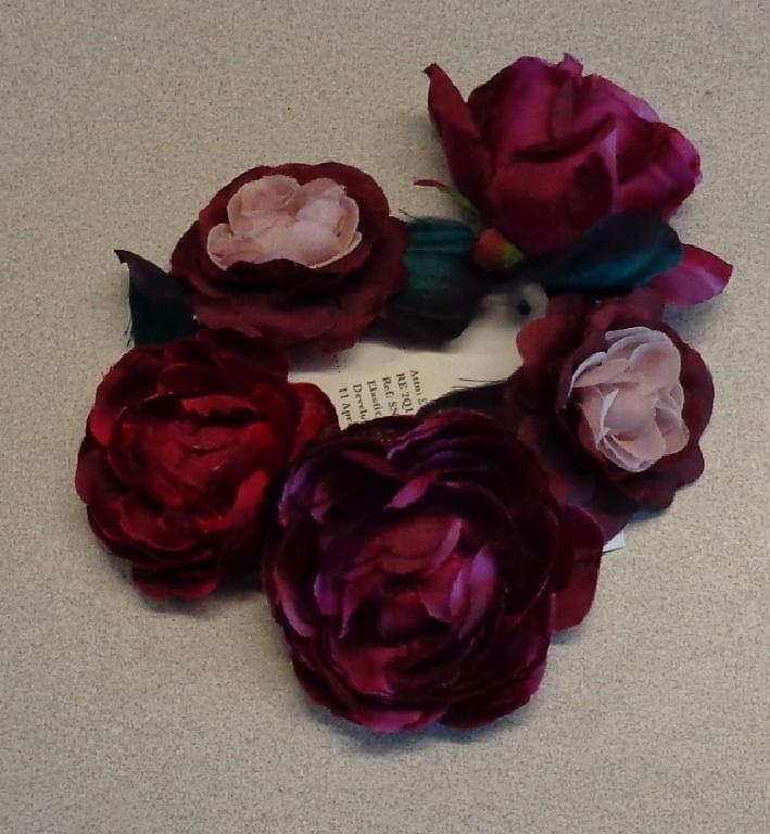 A CIRCULAR HAIR BAND MADE FROM ELASTIC AND TEXTILE. DECORATED WITH FIVE TEXTILE FLOWERS. THE FLOWER'S PETALS HAVE BEEN GLUED INTO PLACE ALONG  WITH A TEXTILE LEAF THEN ATTACHED TO THE BAND BY GLUE USING A SMALL PIECE OF FELT TO HOLD THEM SECURELY IN POSITION. USED TO KEEP A BUN HAIRSTYLE IN PLACE AND TO DECORATE THE HAIR.