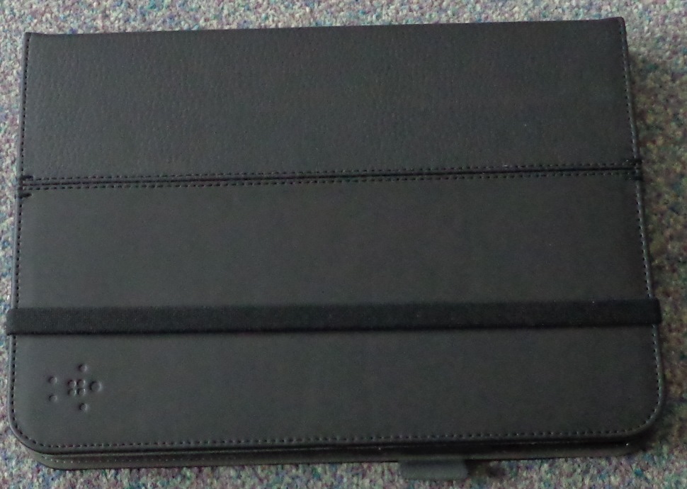 A BLACK LEATHER TABLET CASE. INSIDE IS A MOULDED BLACK PLASTIC TRAY FOR THE TABLET TO SIT IN, WITH INSERTS CUT OUT TO ALLOW ACCESS TO BUTTONS ON THE TABLET, WITH A SMALL HOLE CUT THROUGH THE PLASTIC TRAY AND LEATHER CASE TO ALLOW THE CAMERA FACILITY TO BE USED. THE TRAY CAN ALSO BE USED AS A STAND. THE INNER CASE SURFACE IS GREY WITH TWO CARD SLOTS. ON THE SIDE OF THE CASE IS A LOOP FOR A PEN OR STYLUS. THE CASE IS SECURED BY A 1 CM WIDE PIECE OF ELASTIC AROUND THE OUTER SURFACE. EXTERNAL SURFACE MEASURES APPROXIMATELY 25 CM X 18 CM. PACKAGED IN A GREEN AND WHITE HALF CARDBOARD SLEEVE WITH BLACK WRITING SUITABLE FOR HANGING DISPLAY.