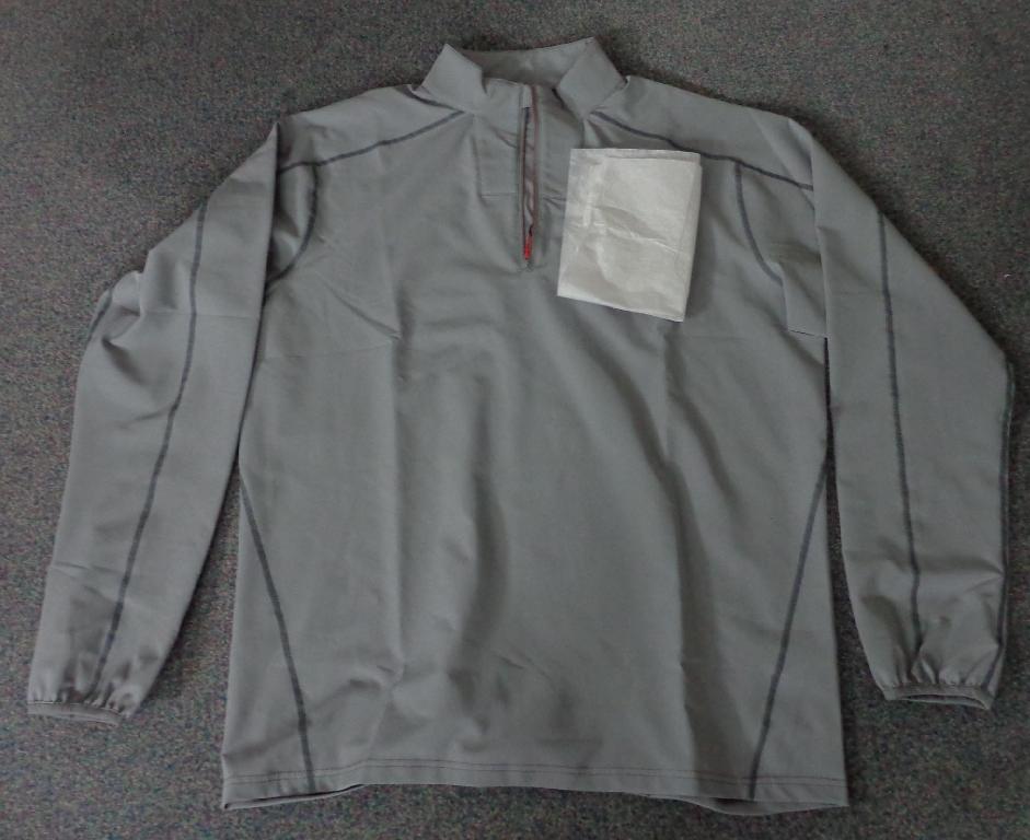 A WOVEN SHIRT-BLOUSE FOR UNISEX. REACHING DOWN TO BELOW THE WAIST. ROUND NECK WITH HIGH STANDING COLLAR. PARTIAL FRONT OPENING WITH ZIP FASTENING.  WITH LONG SLEEVES WITH ELASTICATED BINDING AT SLEEVE ENDS. HEMMED  AT THE BASE. COMPANY LOGOS ON THE FRONT, BACK AND ON THE LOWER RIGHT SLEEVE.

OF 100% POLYESTER WITH INNER WICKING CONSTRUCTION.  SAID TO HAVE A DURABLE WATER REPELLENT OUTER FINISH NOT CONSIDERED VISIBLE TO THE NAKED EYE.