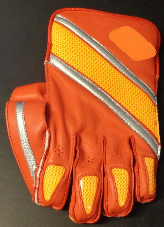 A LEATHER WICKET KEEPER CRICKET GLOVE WITH AN ORANGE RUBBER SHEET WITH MINIATURE RAISED SUCTION CUPS GLUED TO THE PALM TO AID CATCHING THE BALL WITHOUT IT SLIPPING. THERE IS A FURTHER 5CM WIDE STRIP OF LEATHER WITH A GLUED RUBBER SHEET THAT IS ATTACHED FROM THE WIDTH OF THE THUMB TO THE WIDTH OF THE FINGER TO STOP THE BALL SLIPPING THROUGH. THE FINGERS HAVE RUBBER THIMBLES INSIDE THE TIPS TO HELP PROTECT THE FINGER TIPS. THE WRIST IS PADDED WITH CASHMILLION. THE GLOVE IS RED IN COLOUR WITH APPROX  3 ½ CM WIDE ORANGE DIAGONAL TEXTILE STRIP ACROSS THE BACK OF THE GLOVE, EITHER SIDE OF THE TEXTILE STRIP IS A 1 CM SILVER STRIP. ALSO ON THE BACK OF THE GLOVE THERE IS A SMALL MATCHING ORANGE TEXTILE PATCH ON EACH FINGER COATED WITH IDENTICAL SIZE OF CLEAR PLASTIC. ON THE CUFF IS THE COMPANY LOGO IN SILVER.