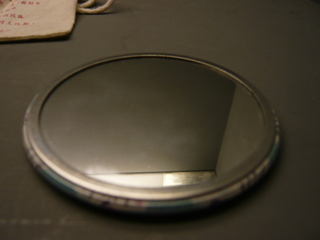 HANDBAG MIRROR PRESENTED IN A COTTON DRAWSTRING PRINTED BAG.
THE MIRROR IS MADE OF GLASS AND IS FRAMED IN A CASING MADE OF ALUMINIUM AND POLYETHELENE PLASTIC. 
THE MIRROR IS ROUND IN SHAPE AND MEASURES 76mm ACROSS.
THE BACK OF THE COMPACT IS PATTERNED.
