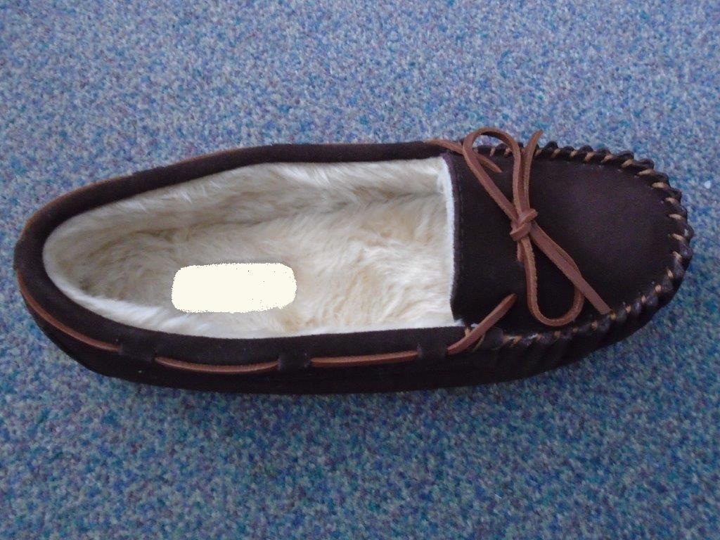LADIES MOCCASIN STYLE SLIP ON SLIPPER, WITH UPPERS OF SUEDE LEATHER AND OUTER SOLES OF RUBBER, WITH A LINING OF FAUX FUR.  NOT COVERING THE ANKLE. CHOCOLATE BROWN IN COLOUR WITH A CONTRASTING LACE AROUND THE TOP LINE THAT TIES ON TOP FRONT OF SLIPPER. WITH A FLAT HEEL. ON THE OUTER SOLE IS A DECORATIVE TREE DESIGN.